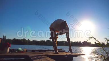 在阳光明媚的日子里，年轻人在湖边练习瑜伽动作和姿势。 体育男子训练
